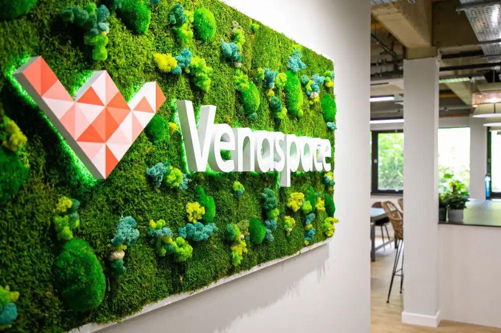 A moss-covered wall sign displaying the Venayopa logo with blue floral accents.